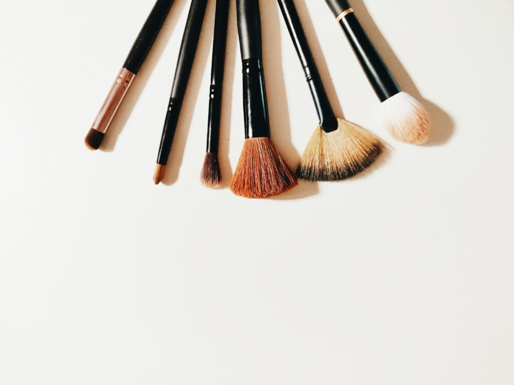A semi-circle arrangement of professional makeup brushes with black handles and mixed brown and white bristles on a white surface.